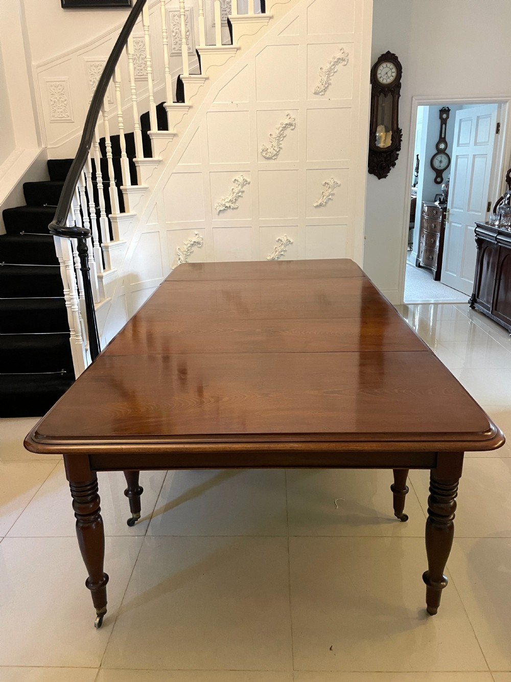 A large Victorian extending mahogany dining table featuring turned legs fitted with brass castors and a polished top with rounded corners.
