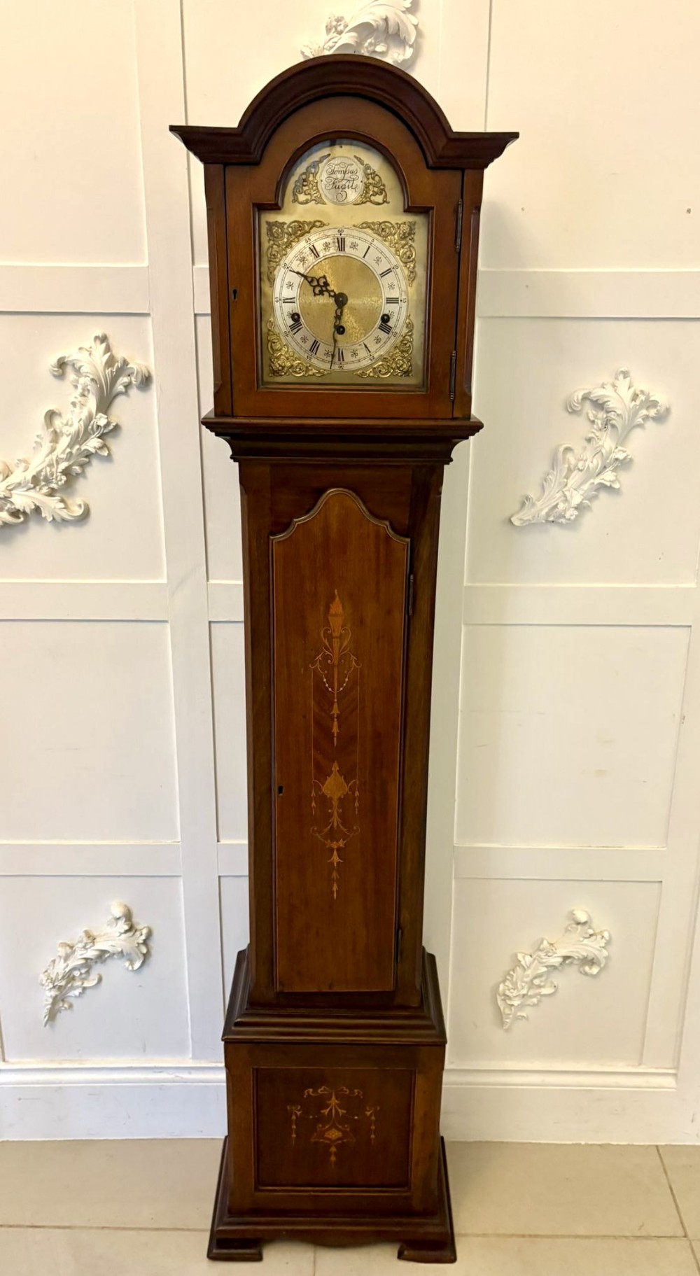 An Edwardian mahogany longcase clock featuring inlaid floral marquetry, an arched hood, and a brass dial with Roman numerals.