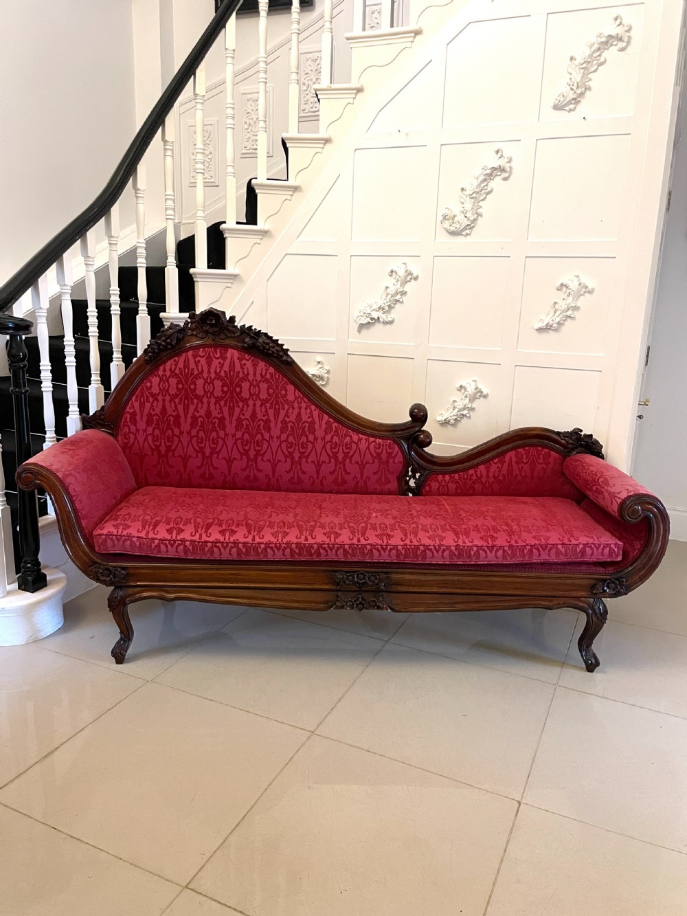 A Victorian carved mahogany chaise longue upholstered in patterned red damask fabric featuring an asymmetrical backrest and carved cabriole legs.