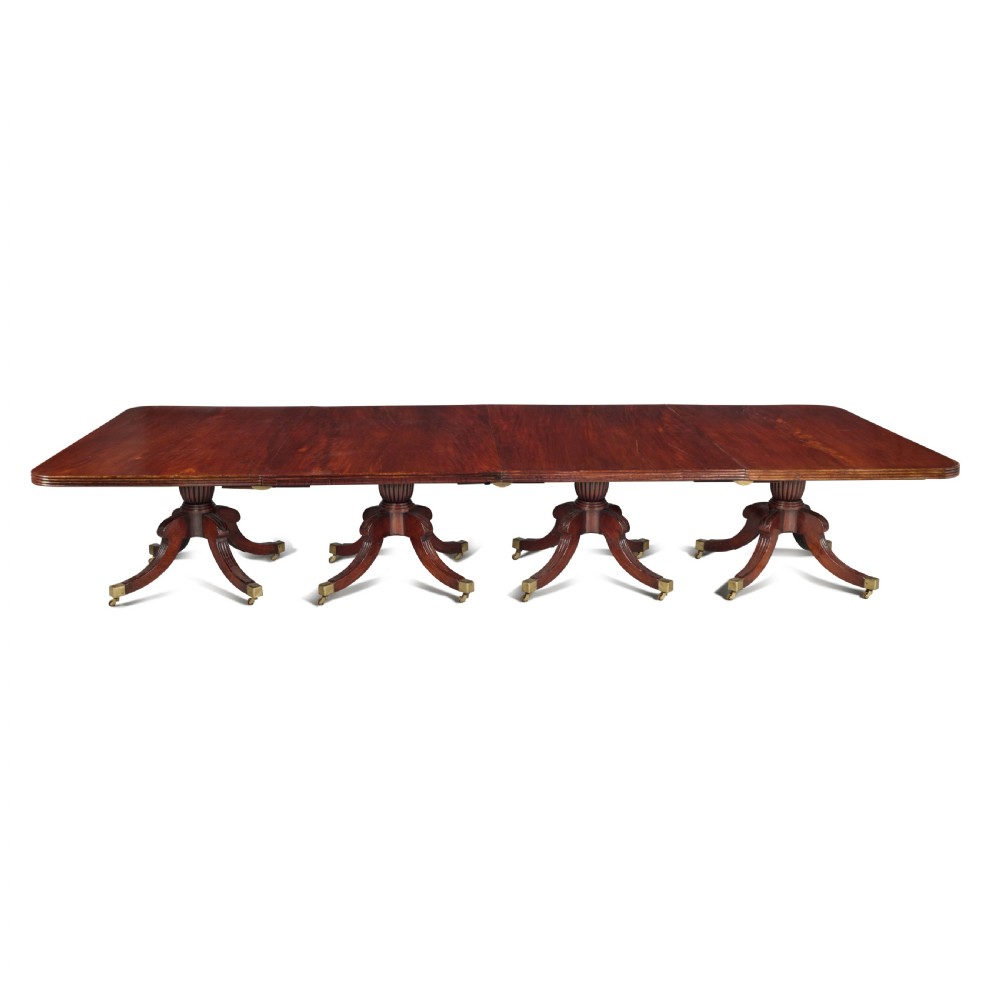 An exceptionally long antique mahogany Regency dining table supported by four reeded pedestal bases with brass castors.