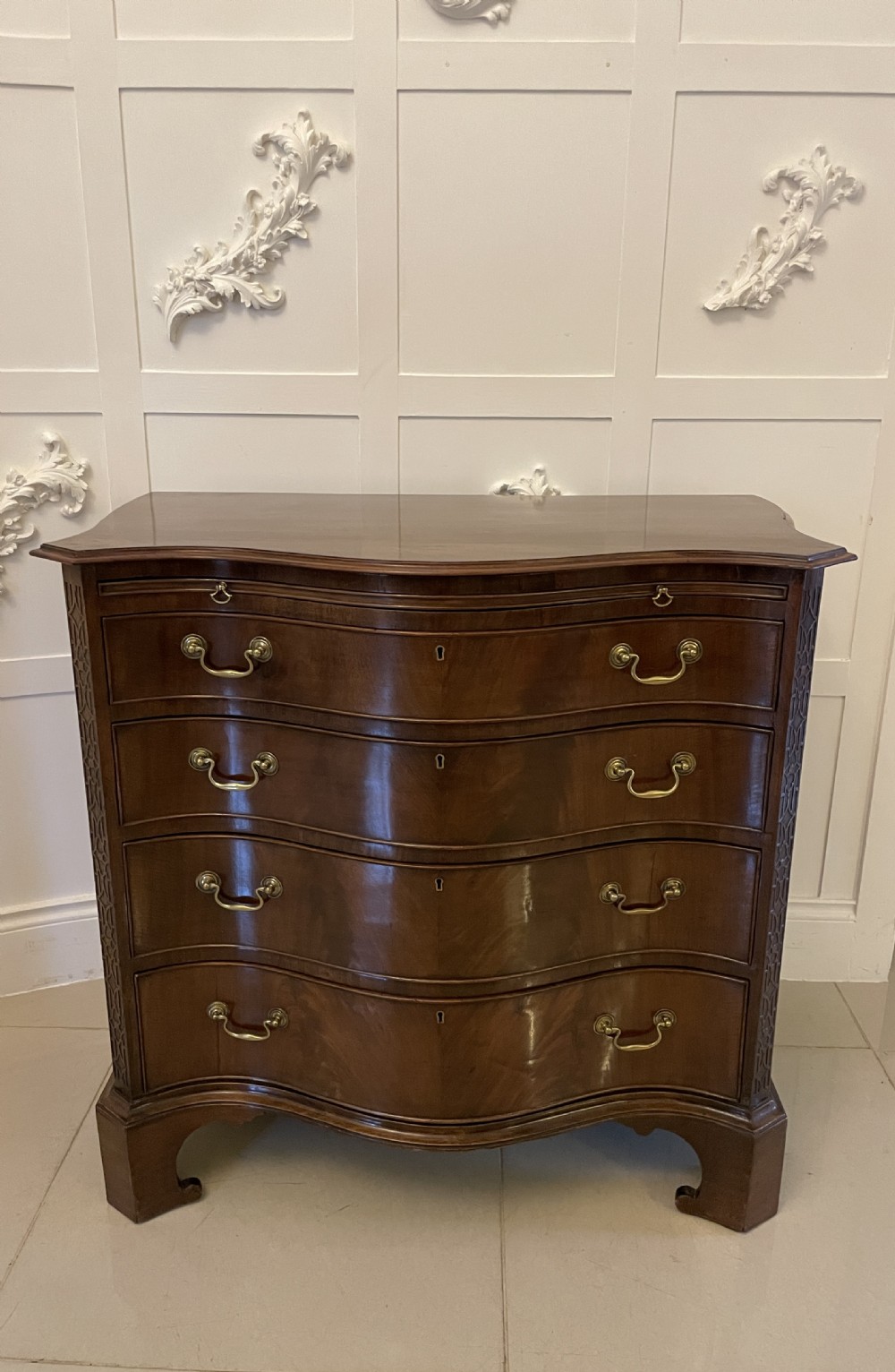 An Edwardian mahogany chest of drawers with a serpentine curved front, four graduated drawers, brass swan-neck handles, and bracket feet.