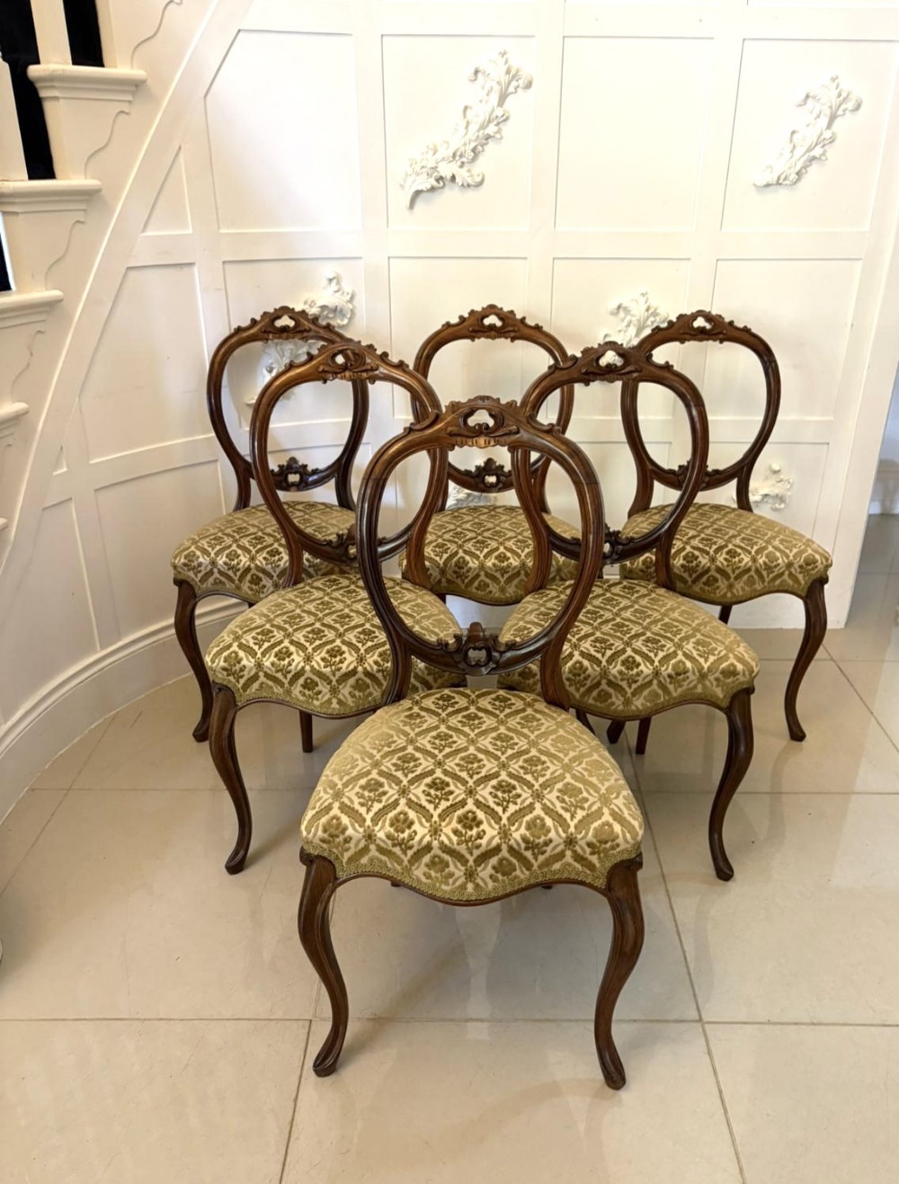 A set of six Victorian carved walnut dining chairs featuring open balloon back frames, patterned green fabric upholstery, and carved cabriole legs.