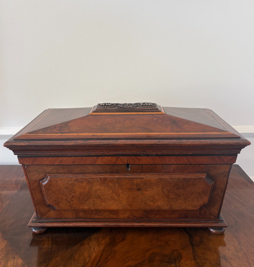 A Victorian burr walnut sarcophagus-shaped tea caddy featuring a carved top plaque, stepped lid, keyhole escutcheon, and small bun feet.