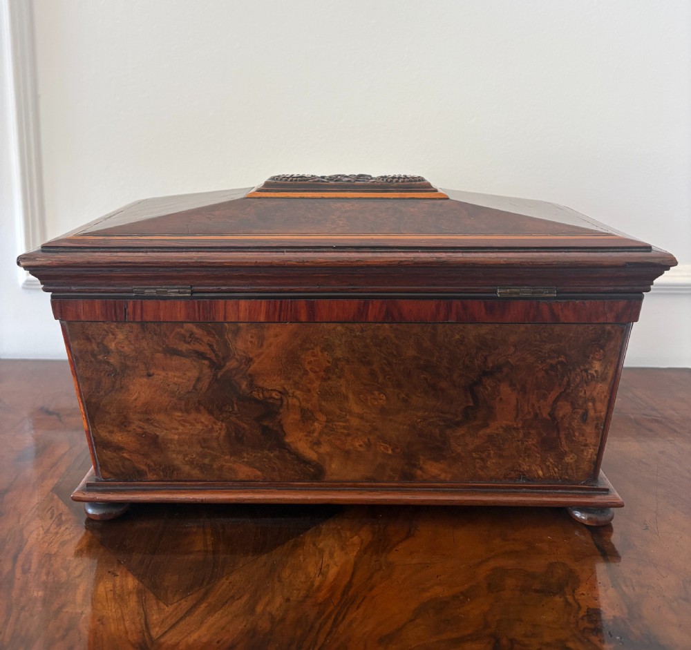A Victorian burr walnut sarcophagus-shaped tea caddy featuring a carved top plaque, stepped lid, keyhole escutcheon, and small bun feet. View IV