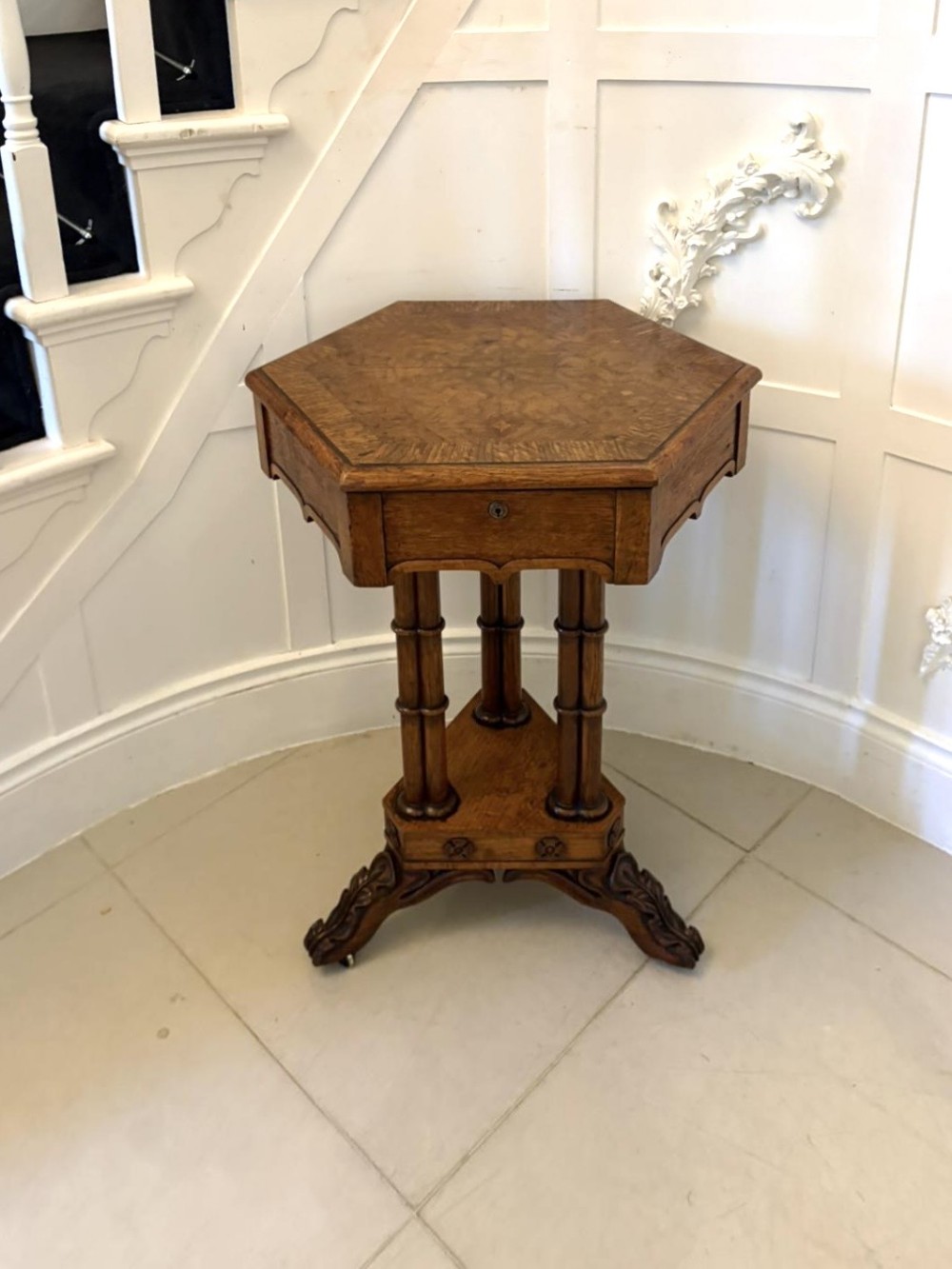 An antique hexagonal pollard oak side table featuring a lift-top lid, ring-turned column supports, and a carved tripartite base with castors.
