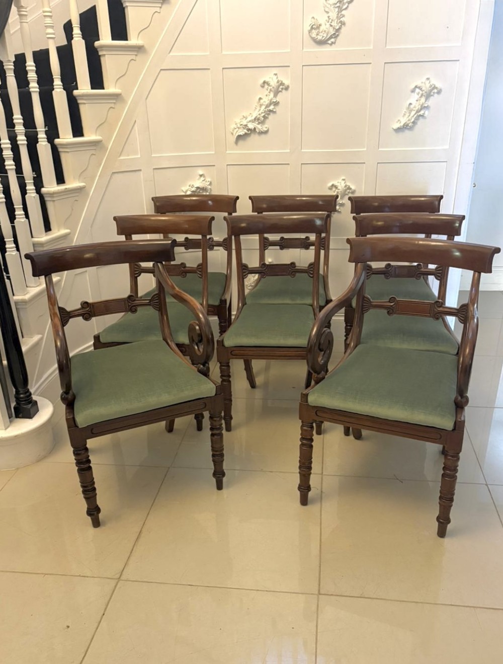 A set of eight antique Regency mahogany dining chairs featuring green velvet upholstery, turned front legs, and two scroll arm carvers.