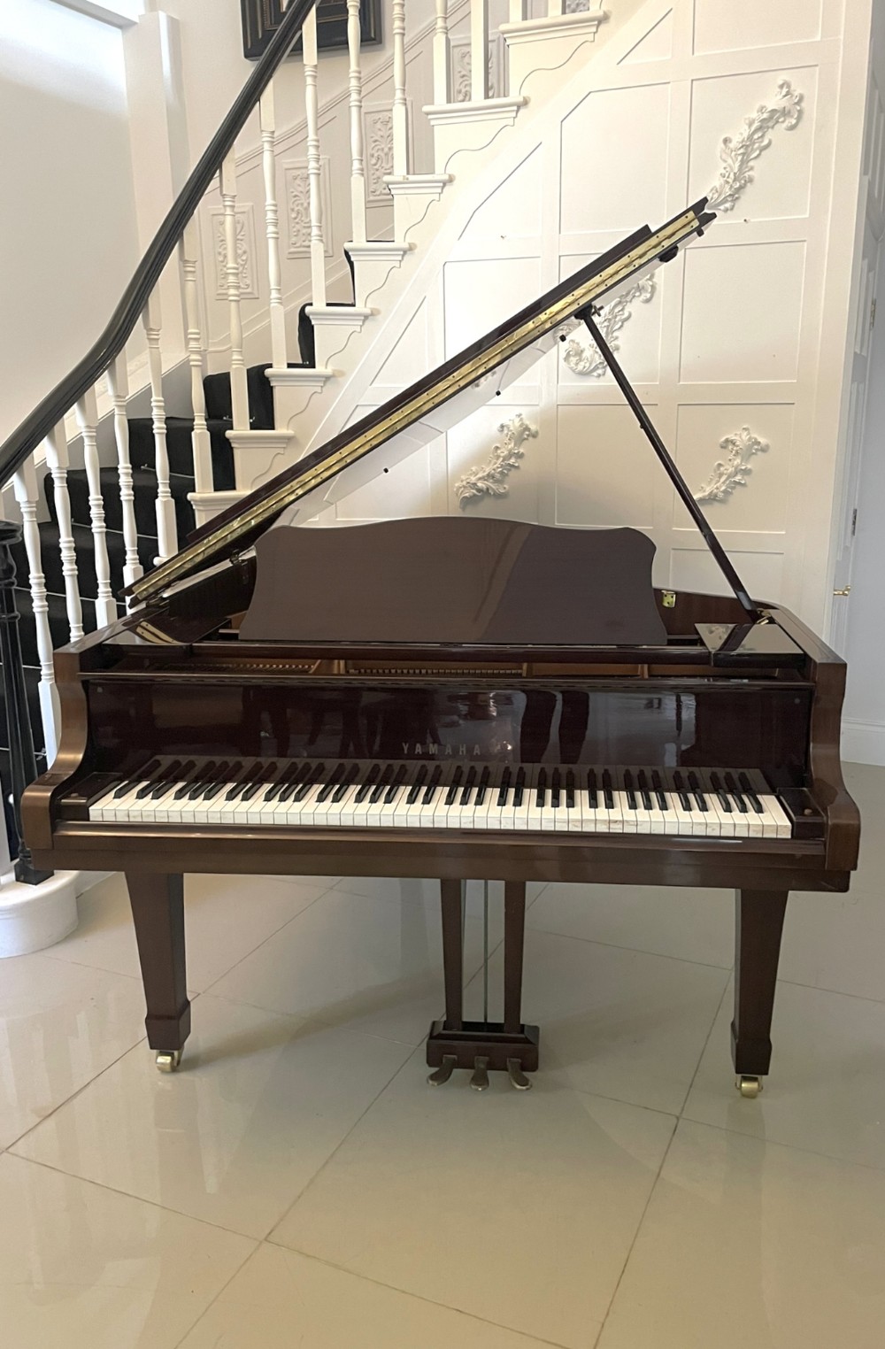 A polished dark mahogany Yamaha baby grand piano shown with its lid propped open, exposing the keys and music stand.