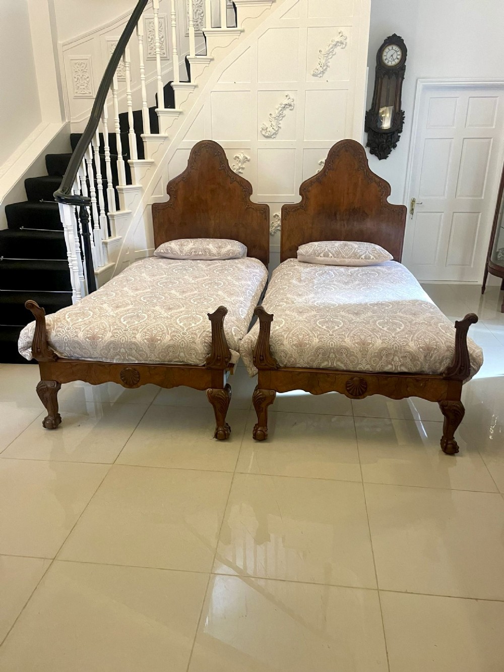 A pair of antique burr walnut single beds featuring high shaped headboards, carved shell detailing on the footboards, and carved cabriole feet.