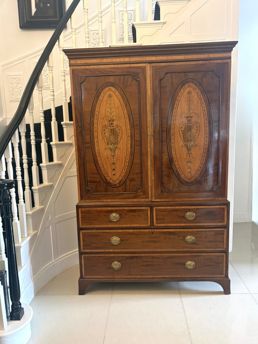An antique Georgian mahogany linen press featuring oval satinwood inlay motifs on two upper doors above four drawers with brass handles.