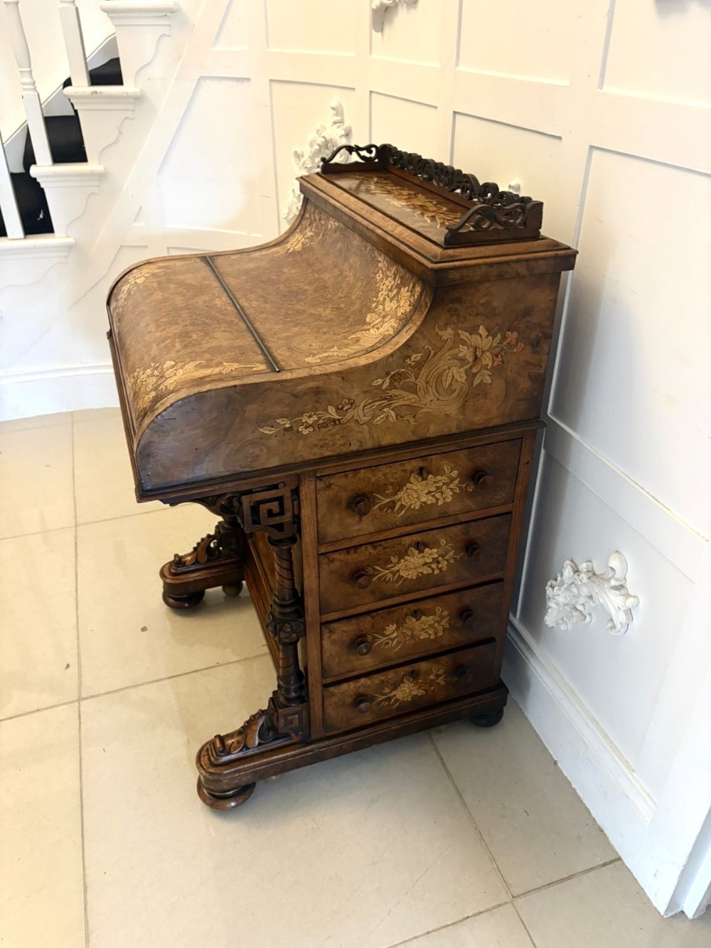 An antique Victorian burr walnut piano top Davenport desk featuring intricate floral marquetry, side drawers, and carved supports.