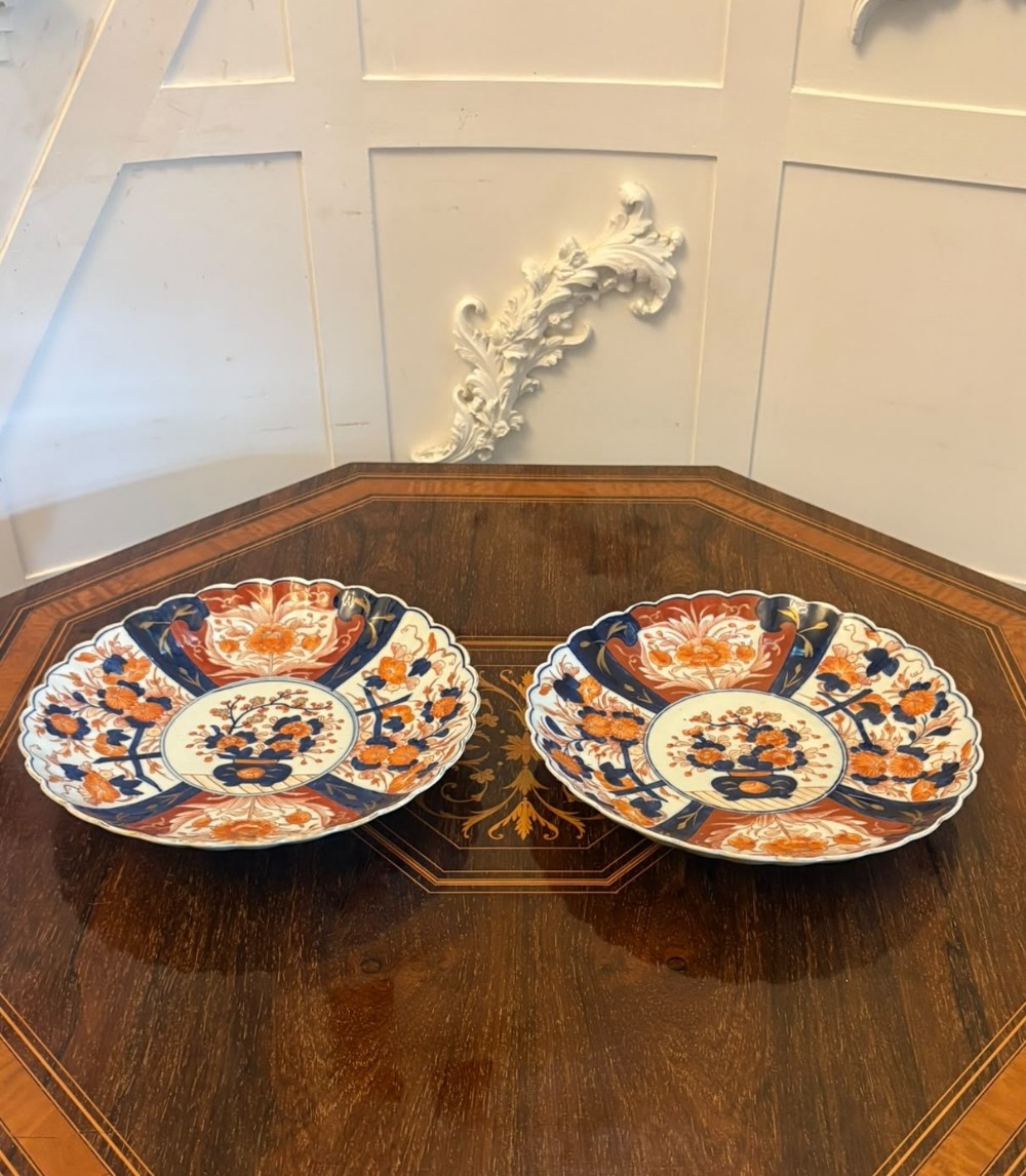 A pair of antique Japanese Imari porcelain plates featuring scalloped edges, cobalt blue and orange floral panels, and a central floral motif.