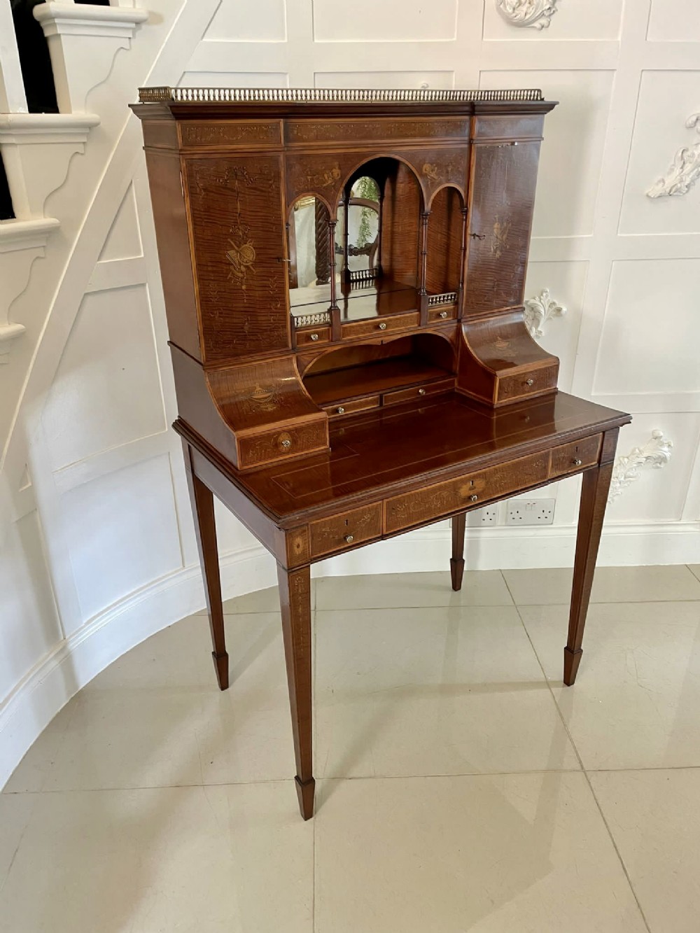 An inlaid mahogany writing desk featuring an elevated superstructure with mirrored arches, floral marquetry, and tapered square legs.