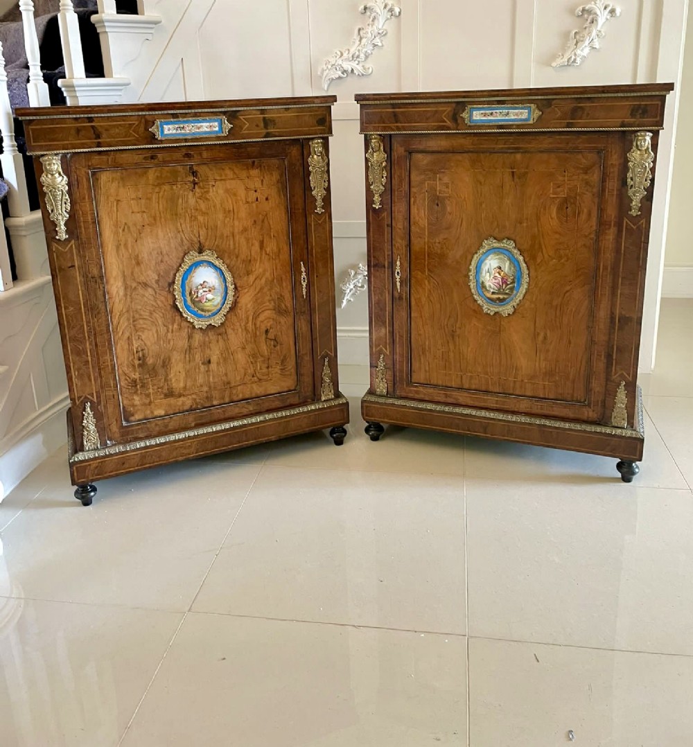 A pair of Victorian burr walnut pier cabinets featuring inlaid stringing, central oval porcelain plaques, and gilt-bronze mounts.