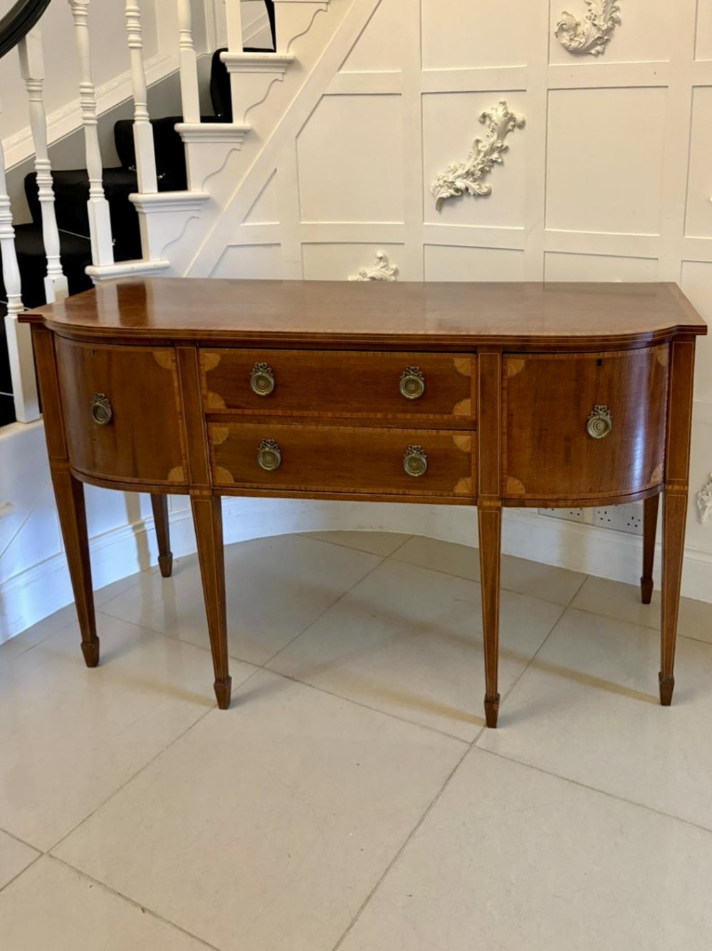 An Edwardian mahogany sideboard featuring satinwood crossbanding, central drawers, side doors, brass ring handles, and square tapered legs.