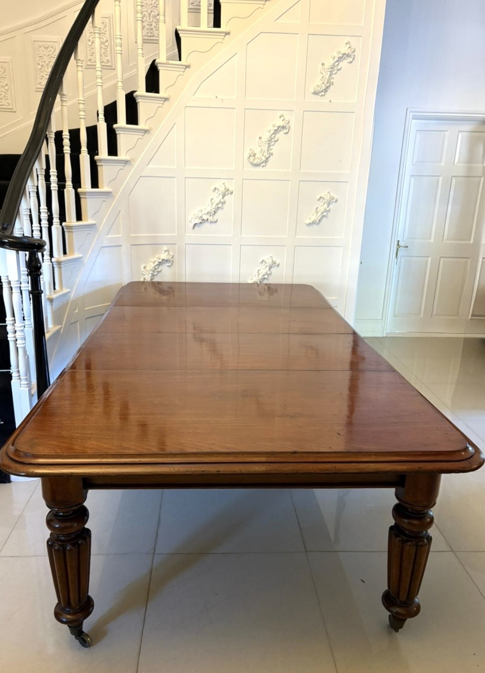 A large Victorian mahogany extending dining table featuring rounded corners, turned fluted legs, and brass castors.