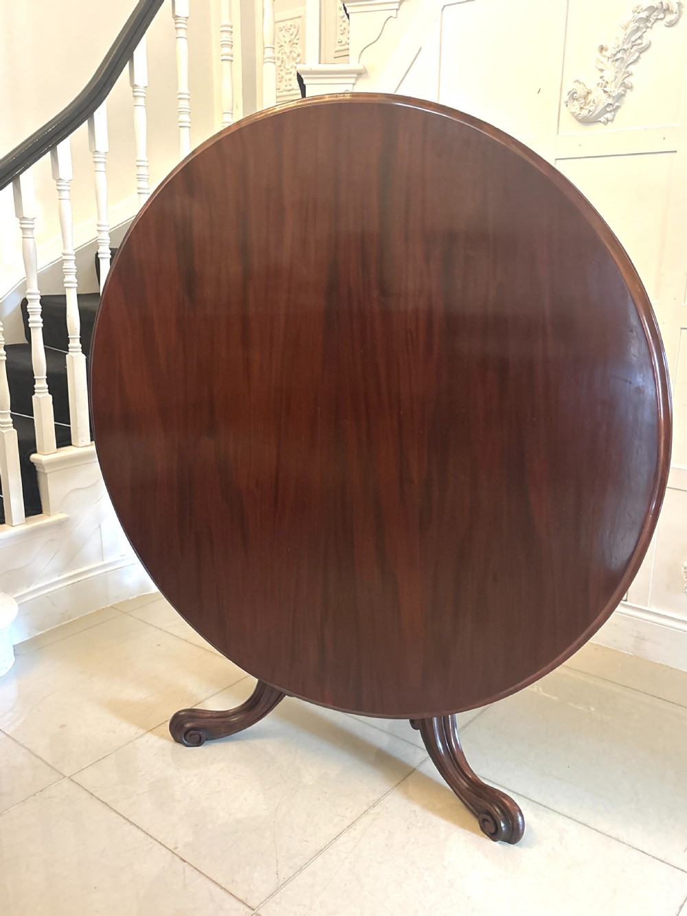 A Victorian circular mahogany tilt-top table shown in the raised vertical position supported on a pedestal base with carved scrolled feet.