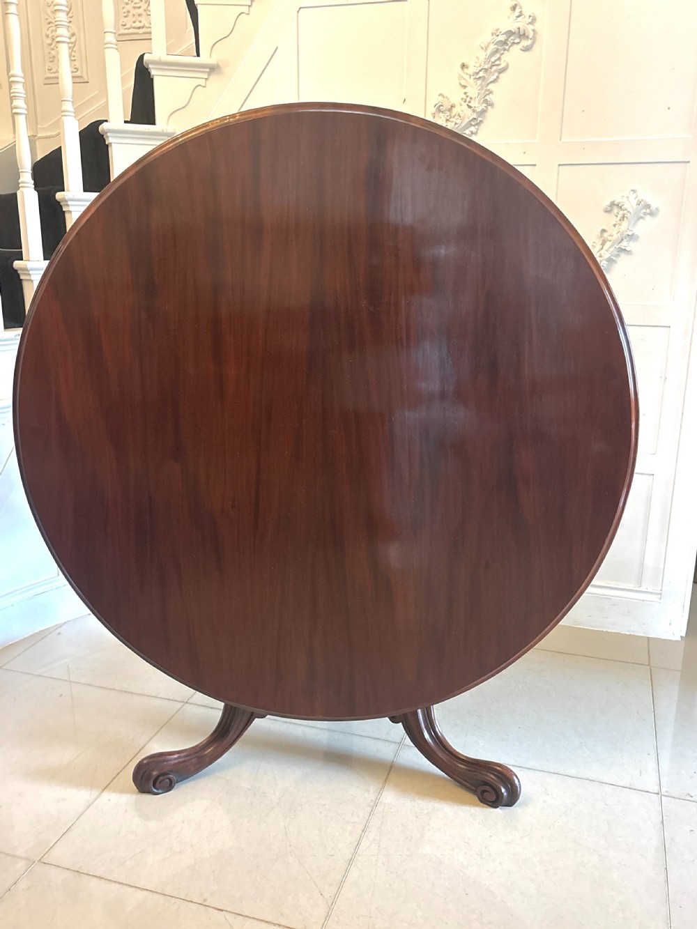A Victorian circular mahogany tilt-top table shown in the raised vertical position supported on a pedestal base with carved scrolled feet. View II