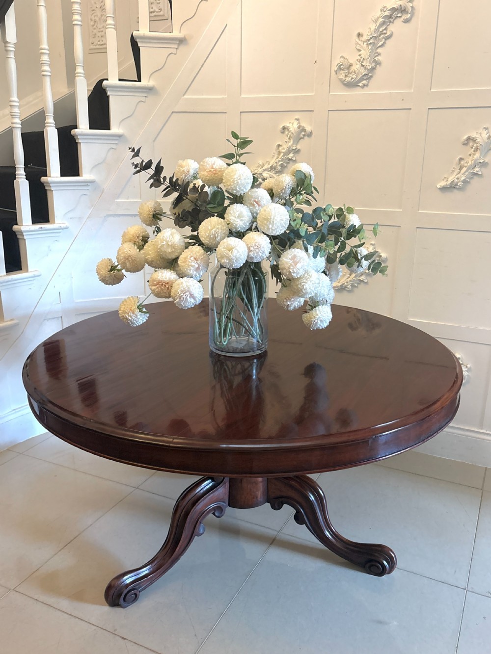 A Victorian circular mahogany tilt-top table shown in the raised vertical position supported on a pedestal base with carved scrolled feet. View III