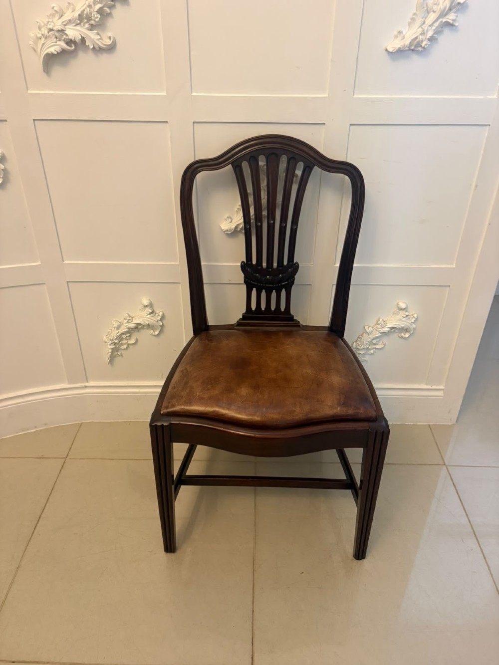 A set of Victorian mahogany Hepplewhite style dining chairs featuring shield-shaped backs with carved splats and tan leather upholstered seats. View IX