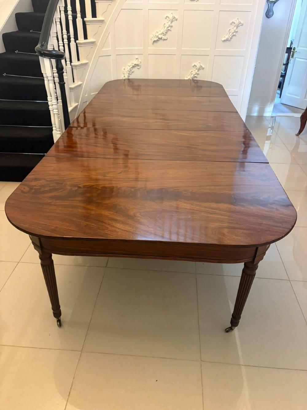 A large, polished Regency mahogany extending dining table with rounded corners and reeded legs fitted with brass castors.