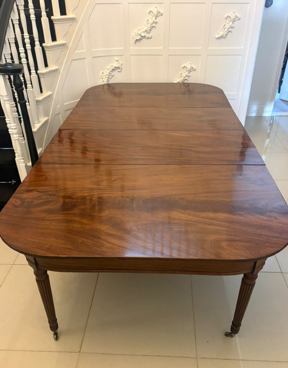 A large, polished Regency mahogany extending dining table with rounded corners and reeded legs fitted with brass castors. View II