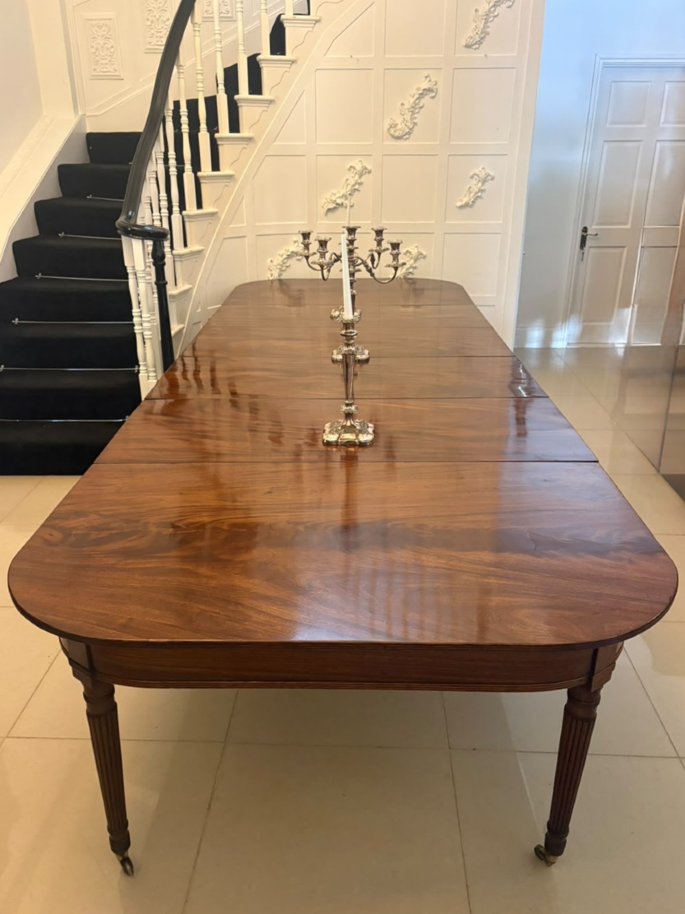 A large, polished Regency mahogany extending dining table with rounded corners and reeded legs fitted with brass castors. View V