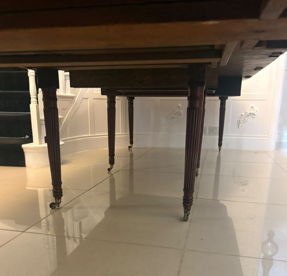 A large, polished Regency mahogany extending dining table with rounded corners and reeded legs fitted with brass castors. View VII