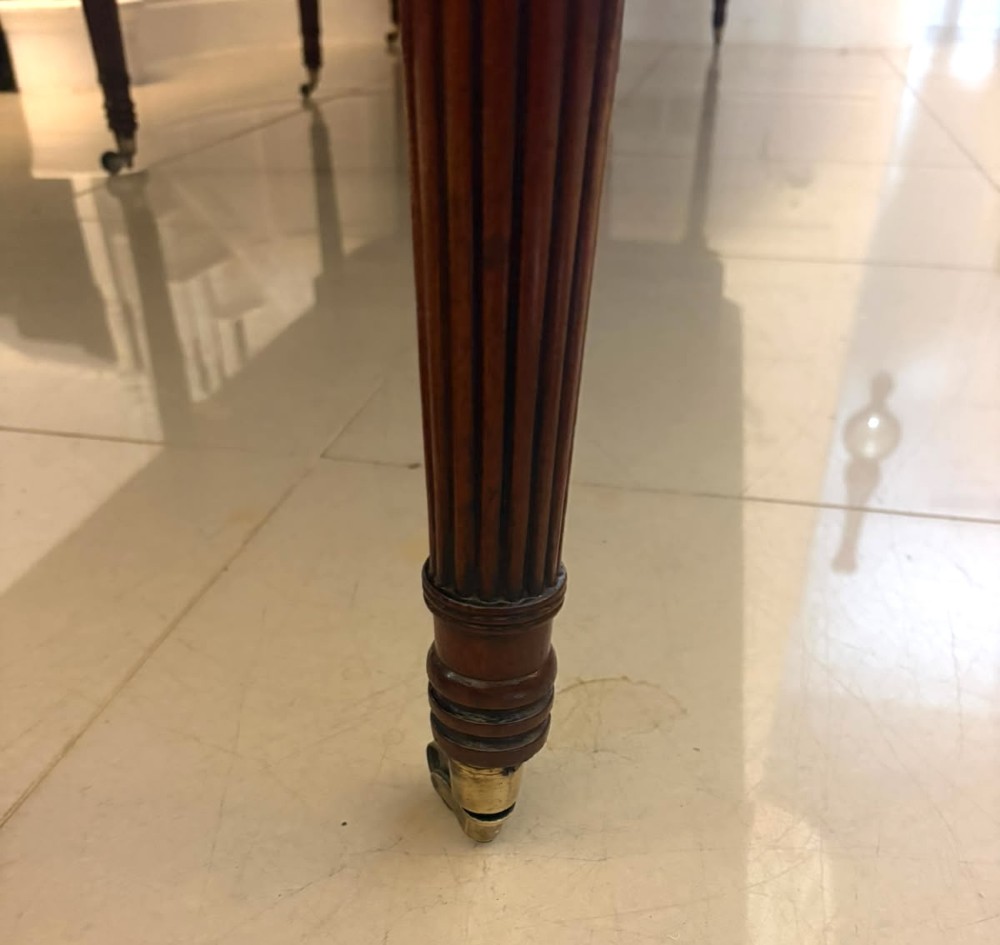 A large, polished Regency mahogany extending dining table with rounded corners and reeded legs fitted with brass castors. View X