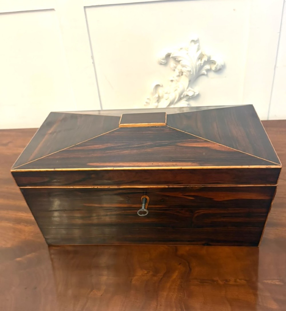 A Regency period dark rosewood tea caddy featuring brass stringing inlay, a faceted lid, and a central keyhole with key inserted.