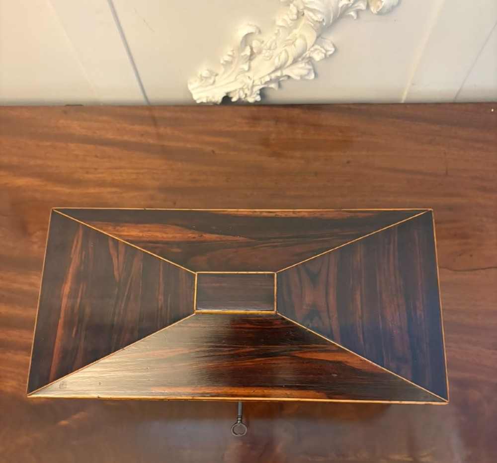 A Regency period dark rosewood tea caddy featuring brass stringing inlay, a faceted lid, and a central keyhole with key inserted. View VI
