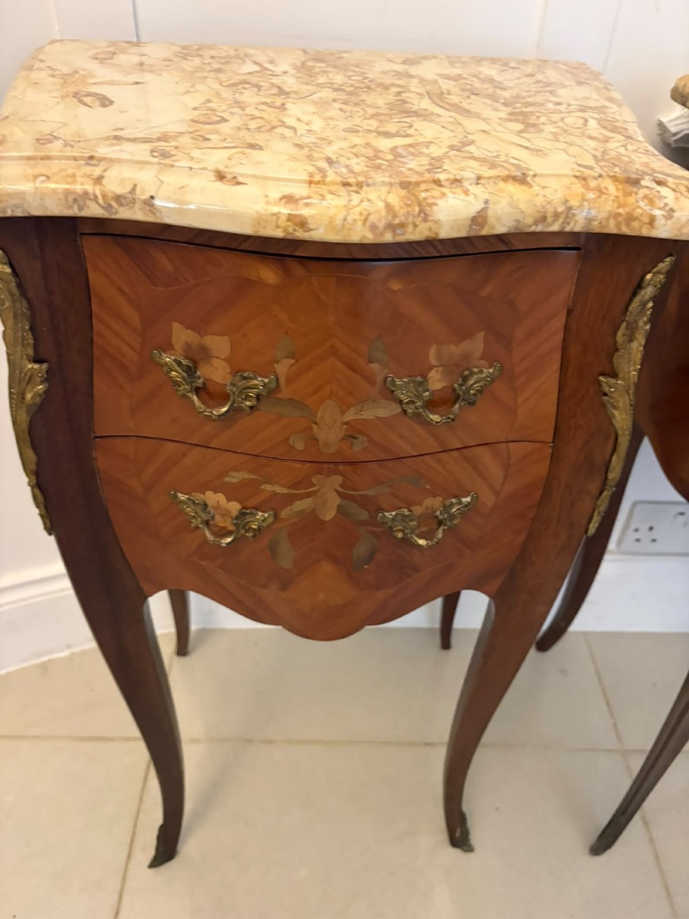 A pair of French Louis XV style kingwood bedside cabinets featuring floral marquetry inlays, gilt bronze mounts, serpentine fronts, and shaped marble tops. View IX