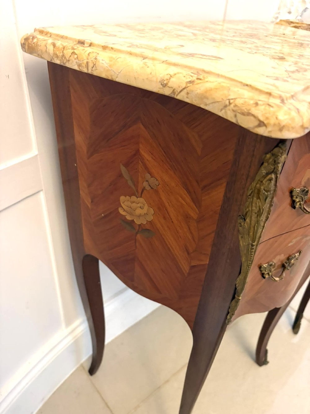 A pair of French Louis XV style kingwood bedside cabinets featuring floral marquetry inlays, gilt bronze mounts, serpentine fronts, and shaped marble tops. View X