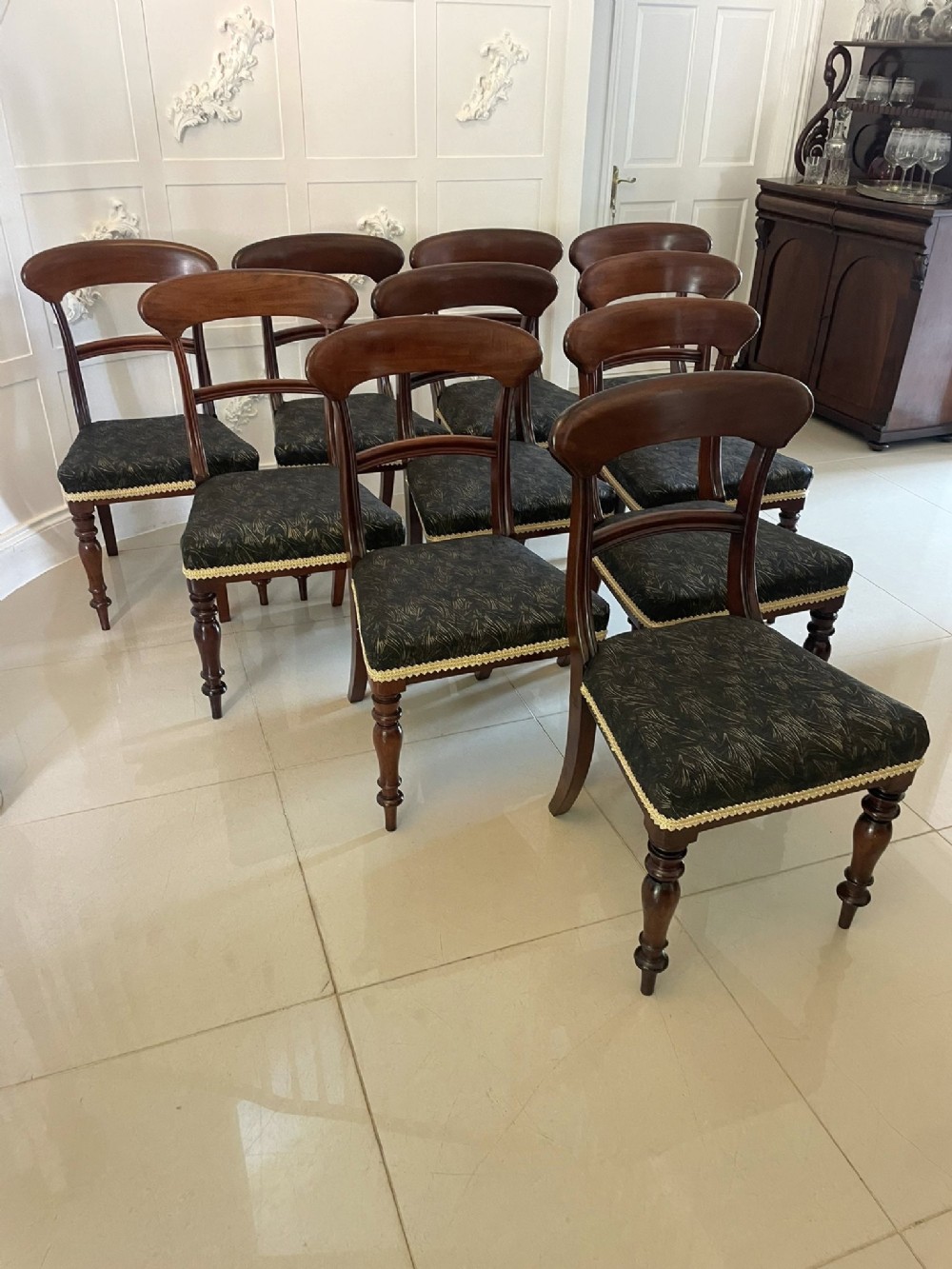 A set of ten Victorian mahogany dining chairs featuring curved top rails, turned front legs, and dark patterned fabric upholstered seats.