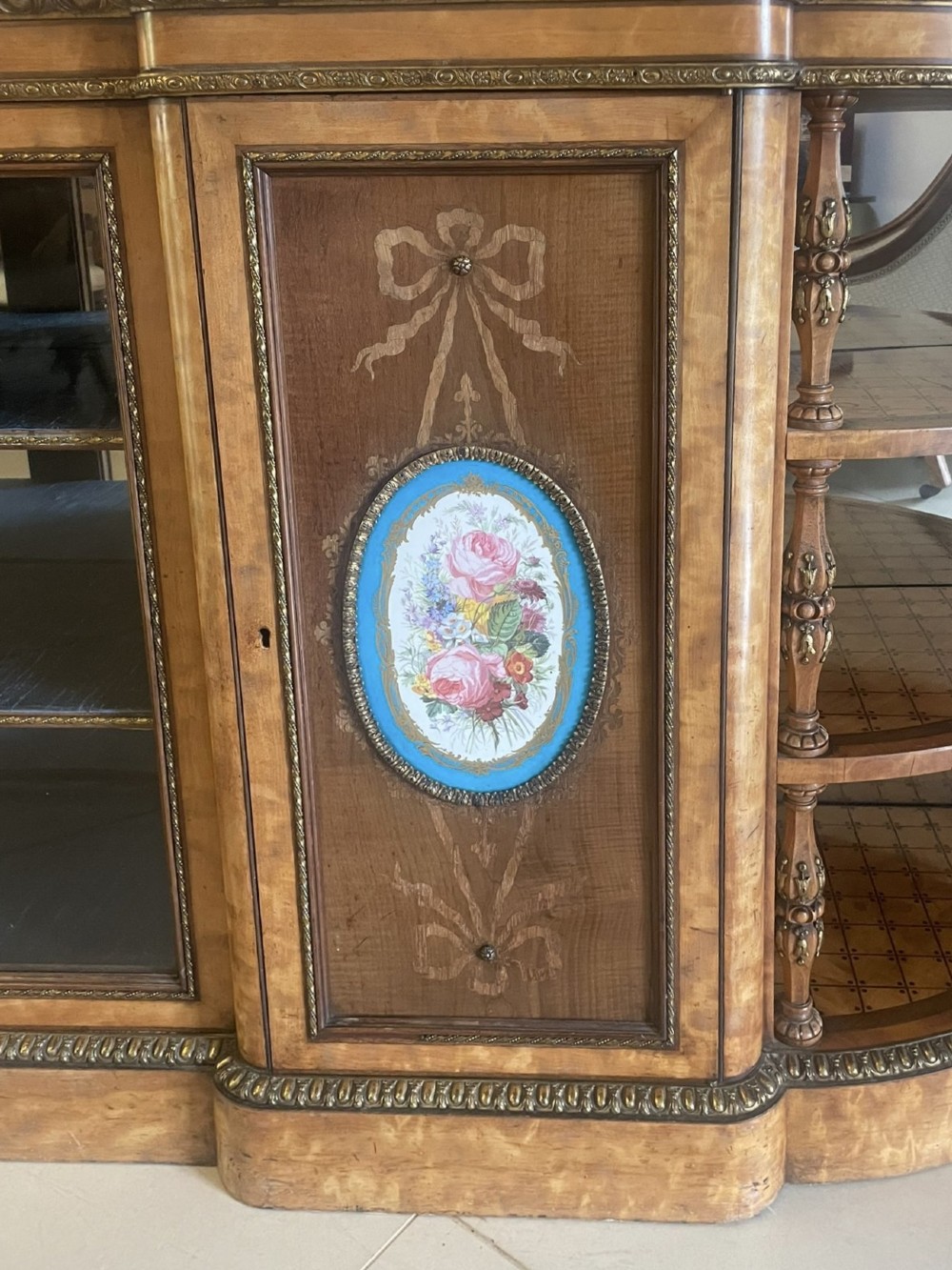 A large Victorian satinwood credenza featuring central glazed doors, oval porcelain plaques, and open curved side shelves. View X
