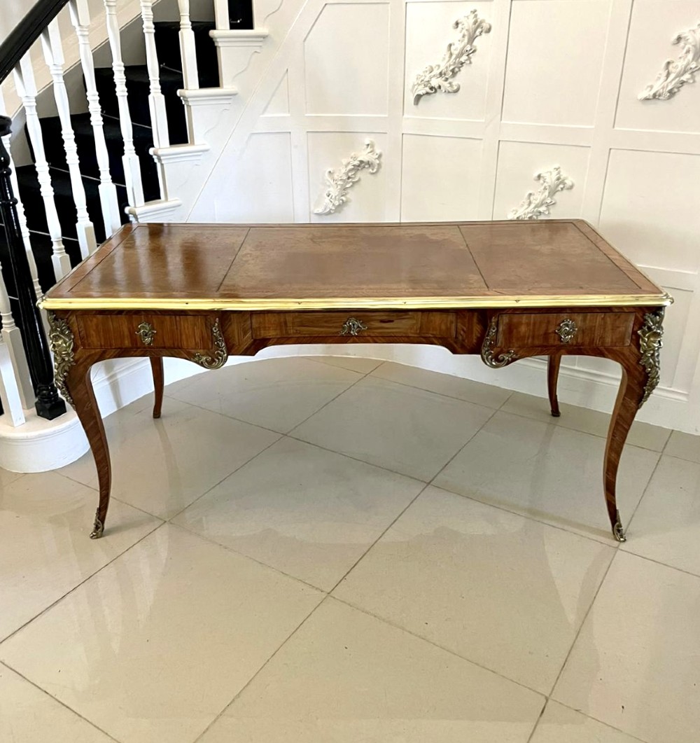A French Louis XV style kingwood bureau plat featuring cabriole legs with ormolu mounts, three frieze drawers, and a leather inset writing surface.