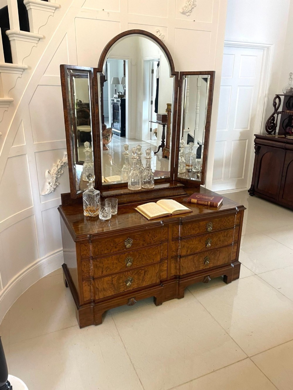 A burr walnut dressing table featuring a central arched triptych mirror, highly figured wood grain, and six drawers with ornate brass handles. View V