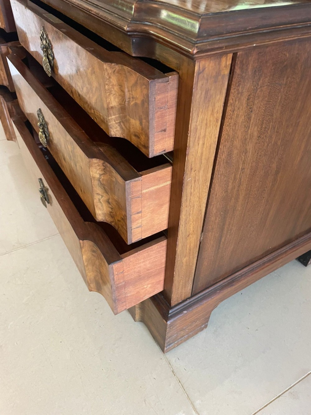 A burr walnut dressing table featuring a central arched triptych mirror, highly figured wood grain, and six drawers with ornate brass handles. View VI