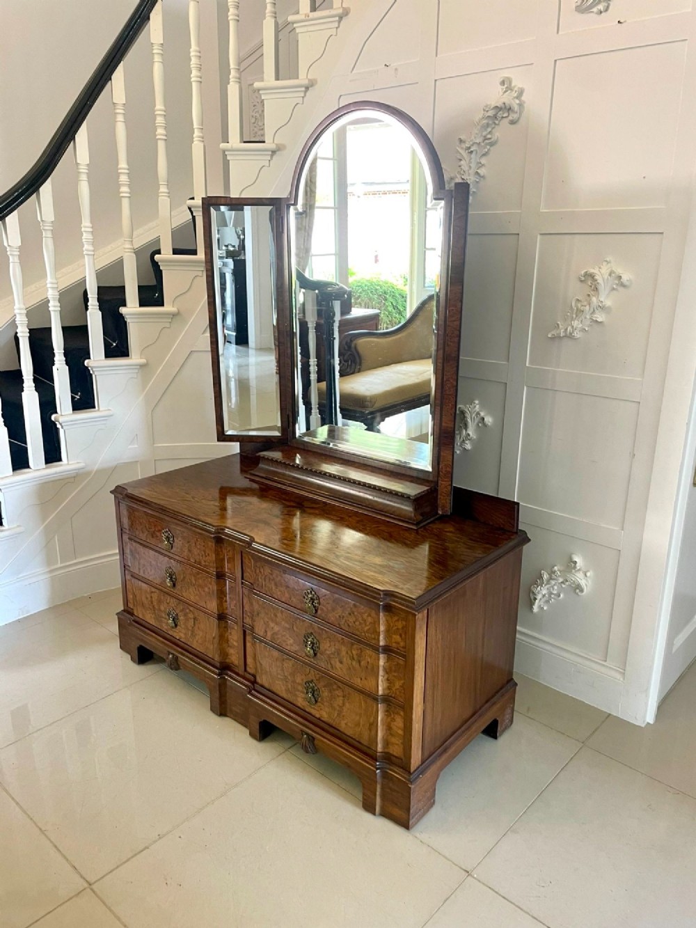 A burr walnut dressing table featuring a central arched triptych mirror, highly figured wood grain, and six drawers with ornate brass handles. View VIII