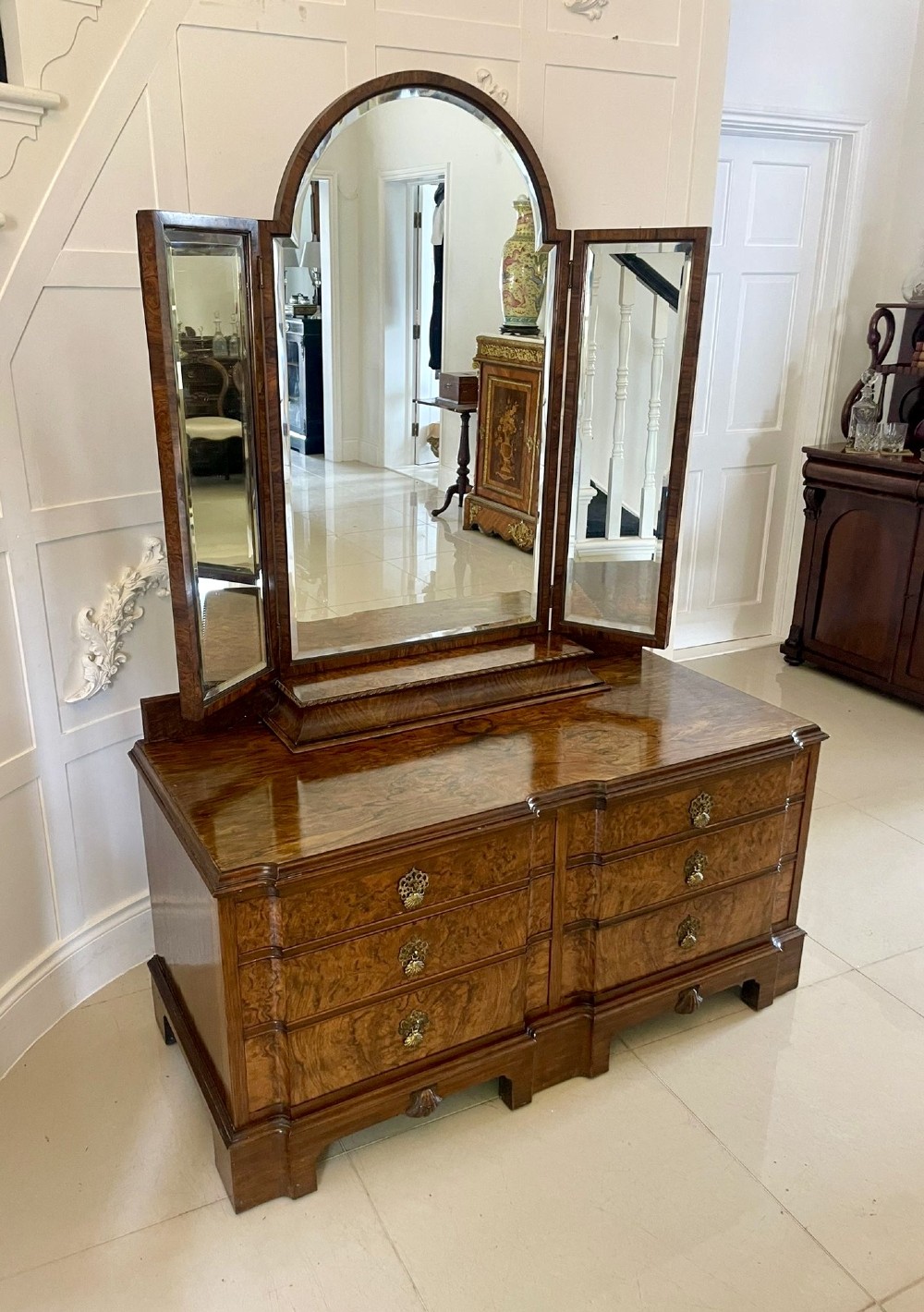 A burr walnut dressing table featuring a central arched triptych mirror, highly figured wood grain, and six drawers with ornate brass handles. View IX