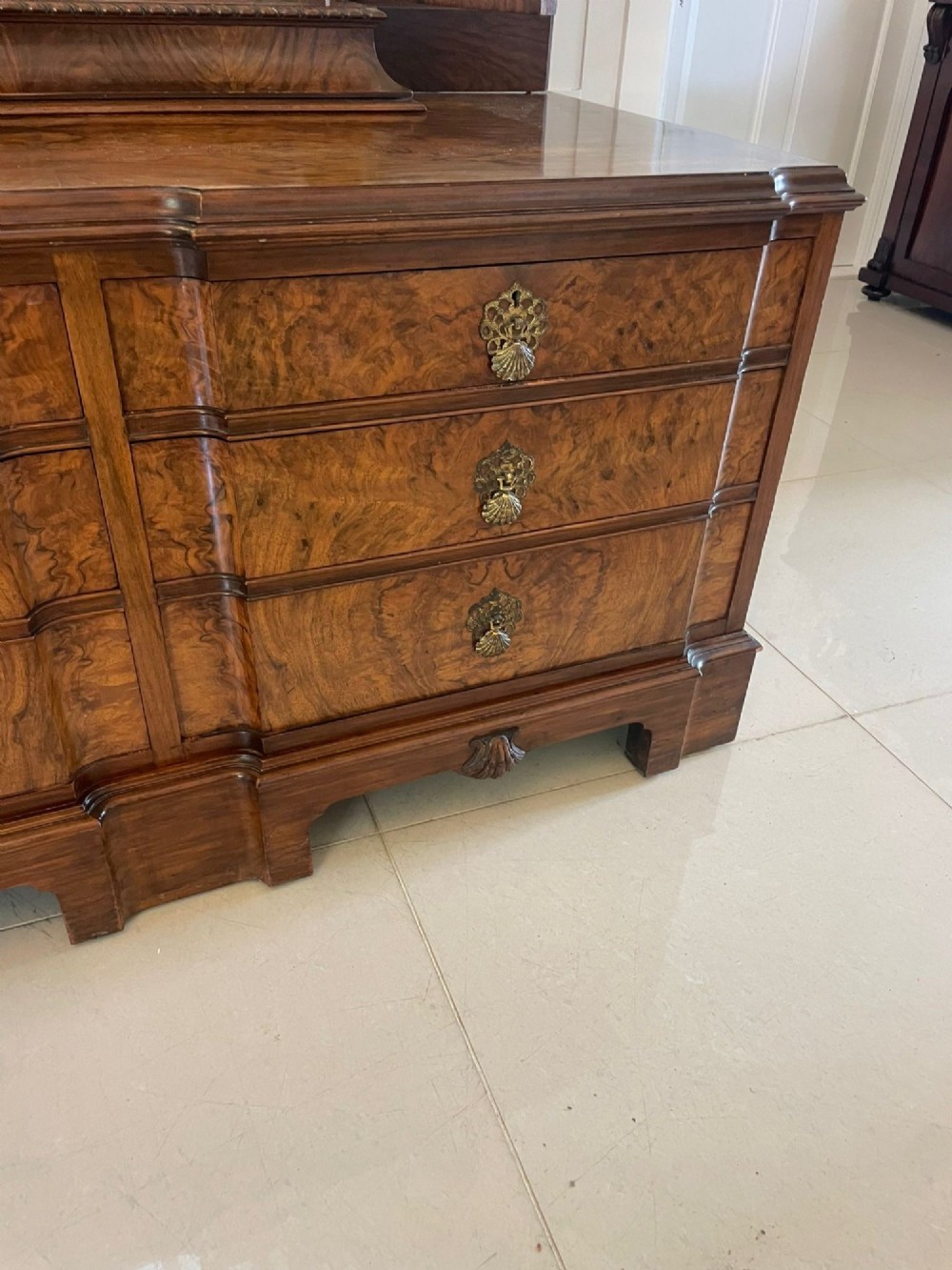 A burr walnut dressing table featuring a central arched triptych mirror, highly figured wood grain, and six drawers with ornate brass handles. View X