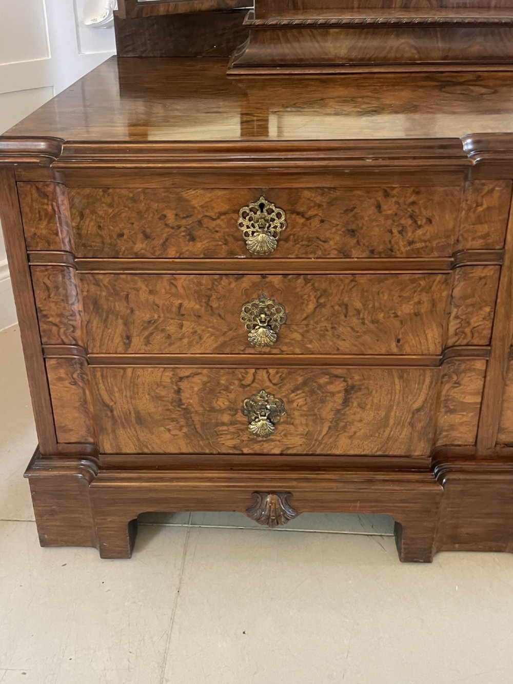 A burr walnut dressing table featuring a central arched triptych mirror, highly figured wood grain, and six drawers with ornate brass handles. View XII