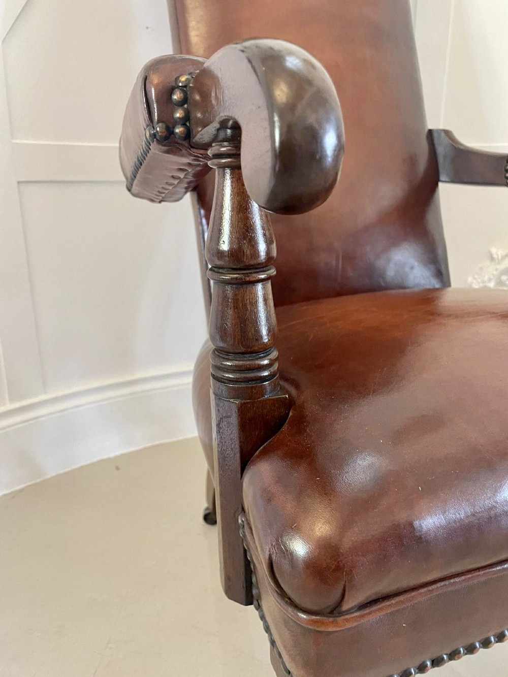 A William IV high-backed armchair upholstered in chestnut brown leather with brass stud detailing, supported by turned mahogany front legs on brass castors. View V