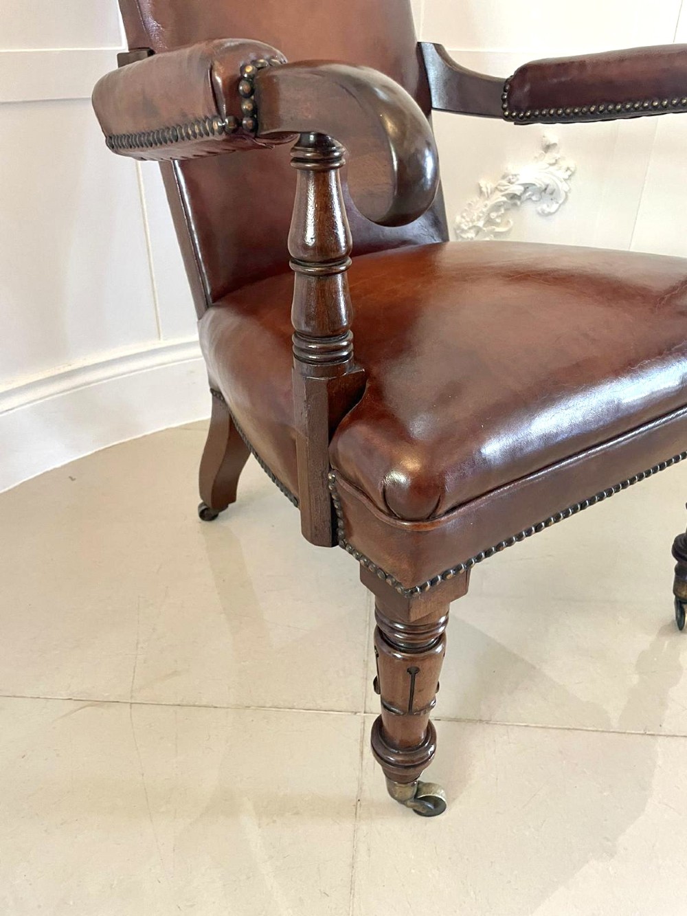 A William IV high-backed armchair upholstered in chestnut brown leather with brass stud detailing, supported by turned mahogany front legs on brass castors. View VI