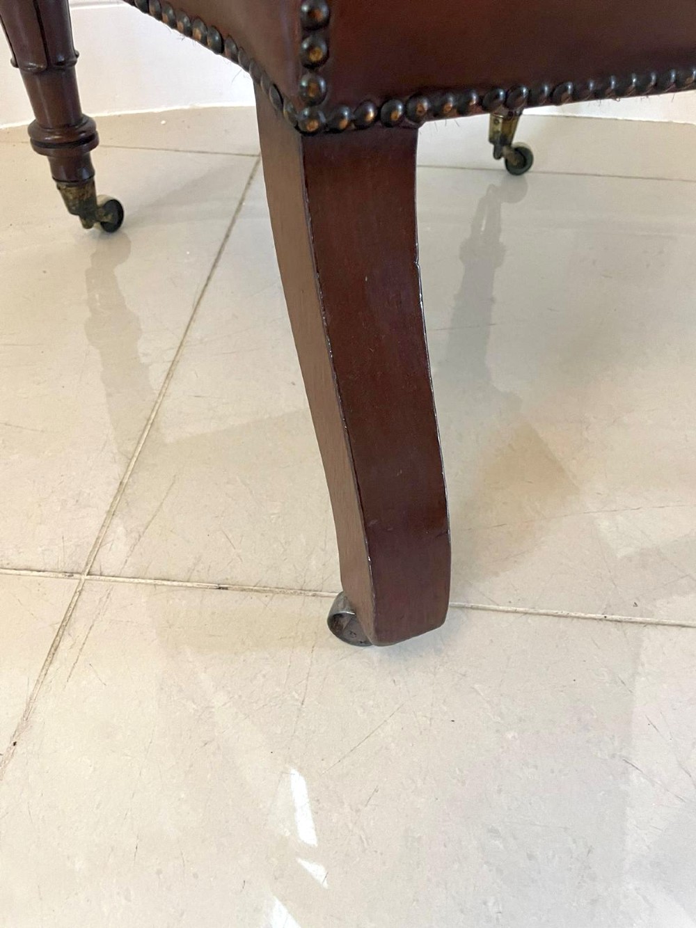 A William IV high-backed armchair upholstered in chestnut brown leather with brass stud detailing, supported by turned mahogany front legs on brass castors. View VIII