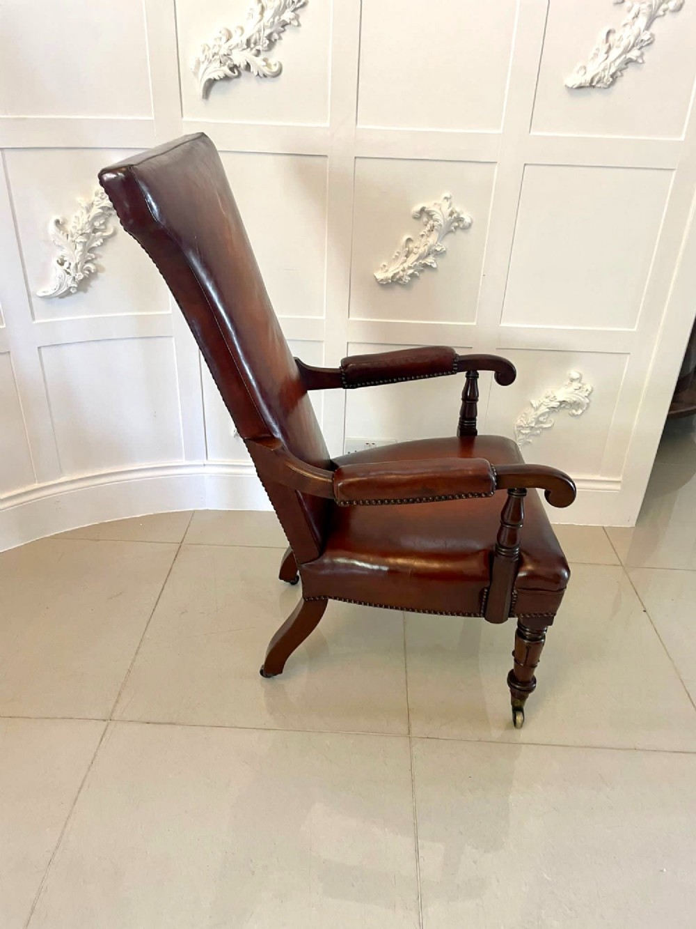 A William IV high-backed armchair upholstered in chestnut brown leather with brass stud detailing, supported by turned mahogany front legs on brass castors. View IX