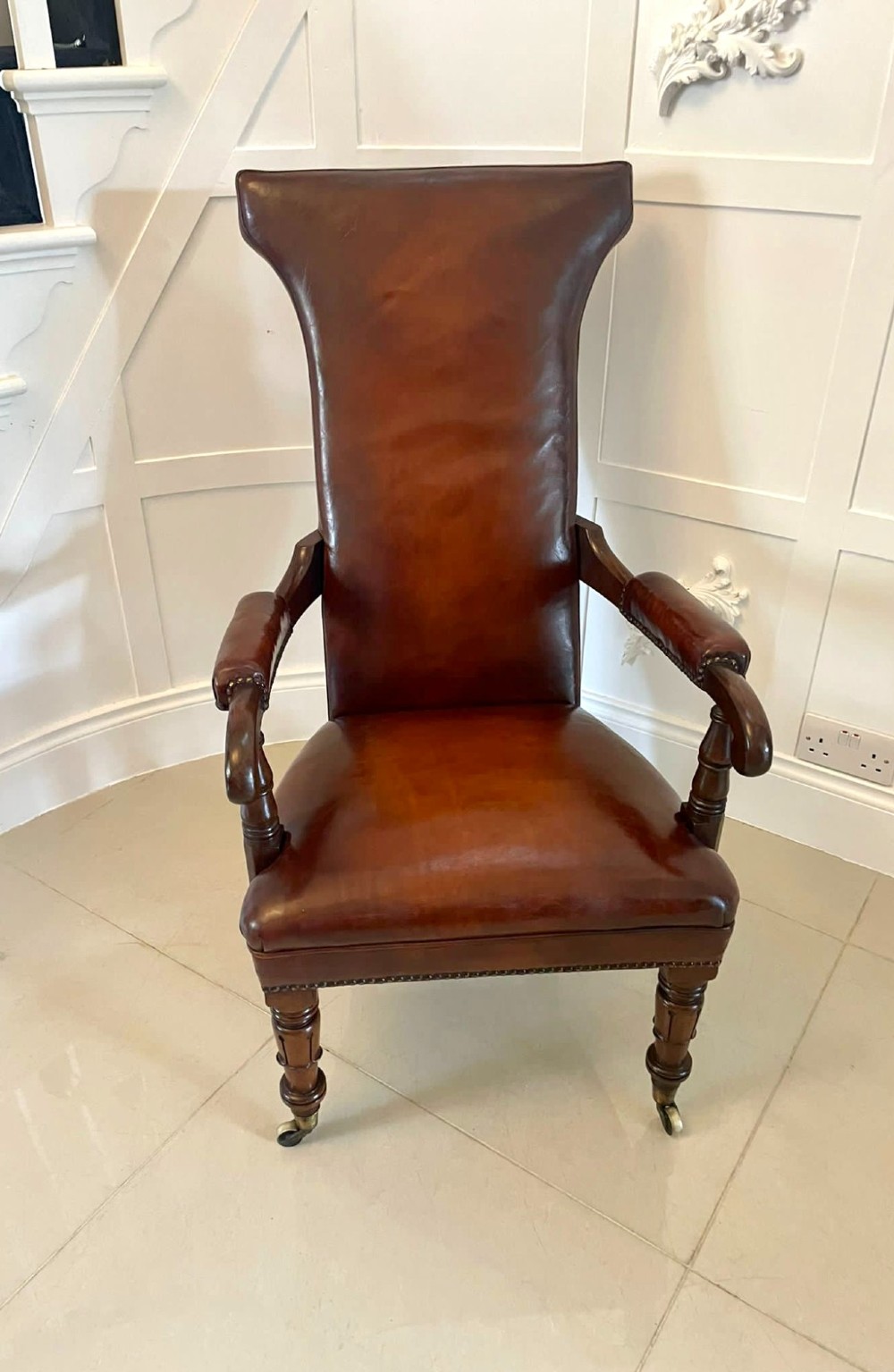A William IV high-backed armchair upholstered in chestnut brown leather with brass stud detailing, supported by turned mahogany front legs on brass castors. View XII