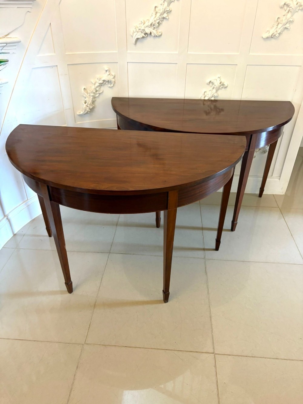 A pair of George III mahogany demi-lune console tables with polished semi-circular tops and tapered square legs.