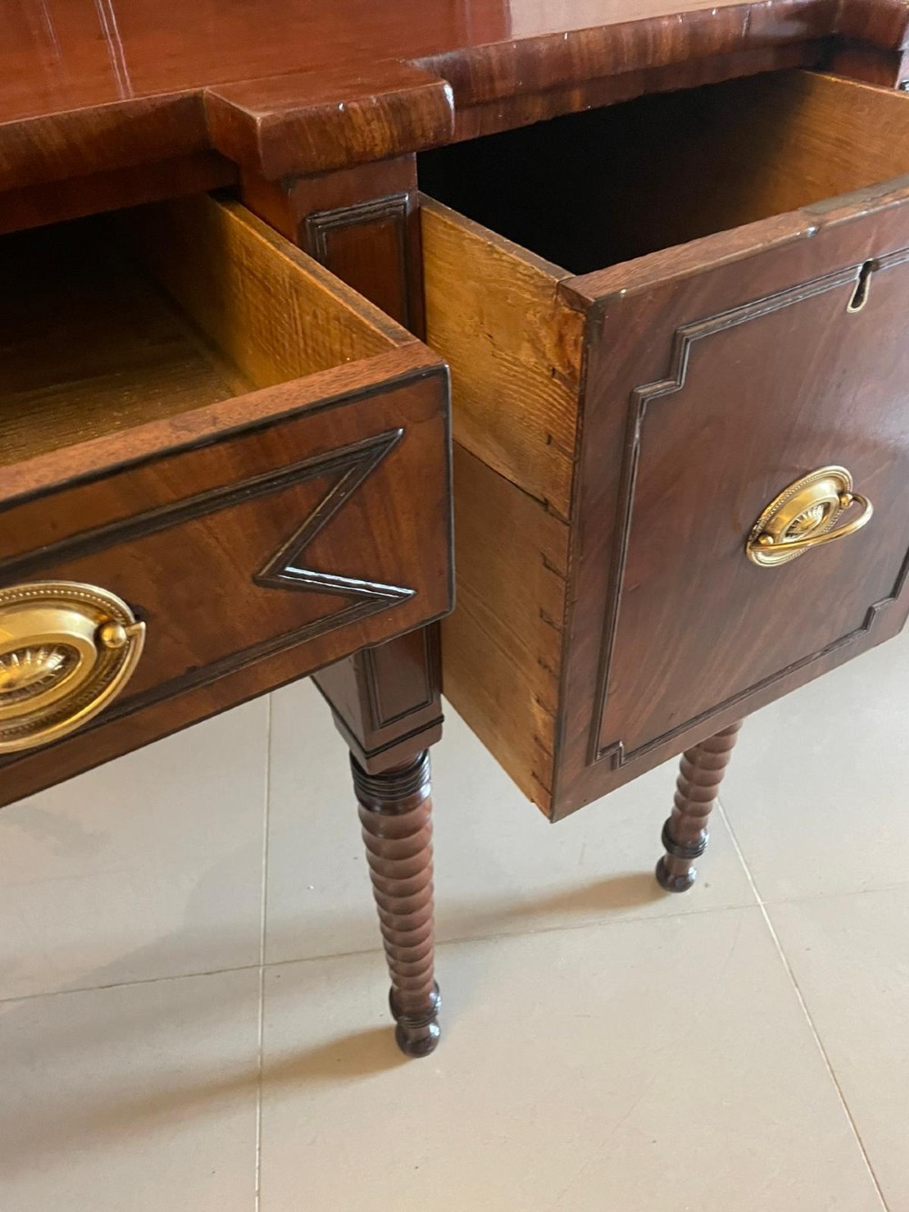 A large George III figured mahogany sideboard featuring a raised gallery, central drawers with brass handles, side cupboards, and turned reeded legs. View II