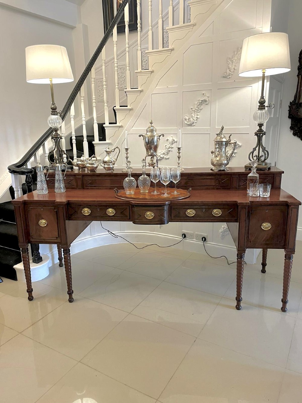 A large George III figured mahogany sideboard featuring a raised gallery, central drawers with brass handles, side cupboards, and turned reeded legs. View IV