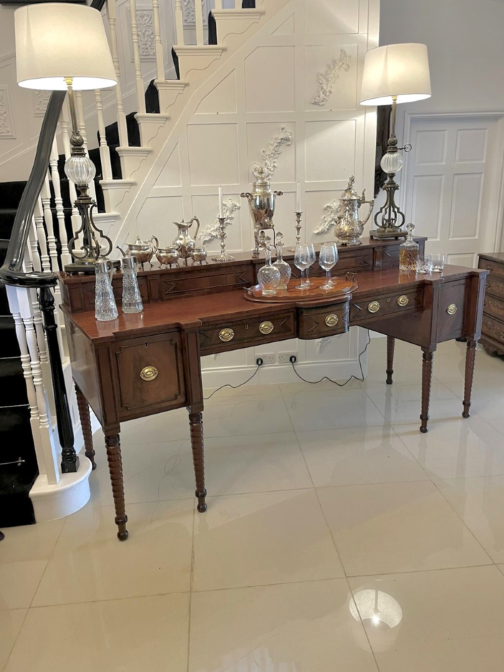 A large George III figured mahogany sideboard featuring a raised gallery, central drawers with brass handles, side cupboards, and turned reeded legs. View V